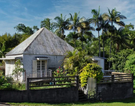 a small house with a fence and trees in the background