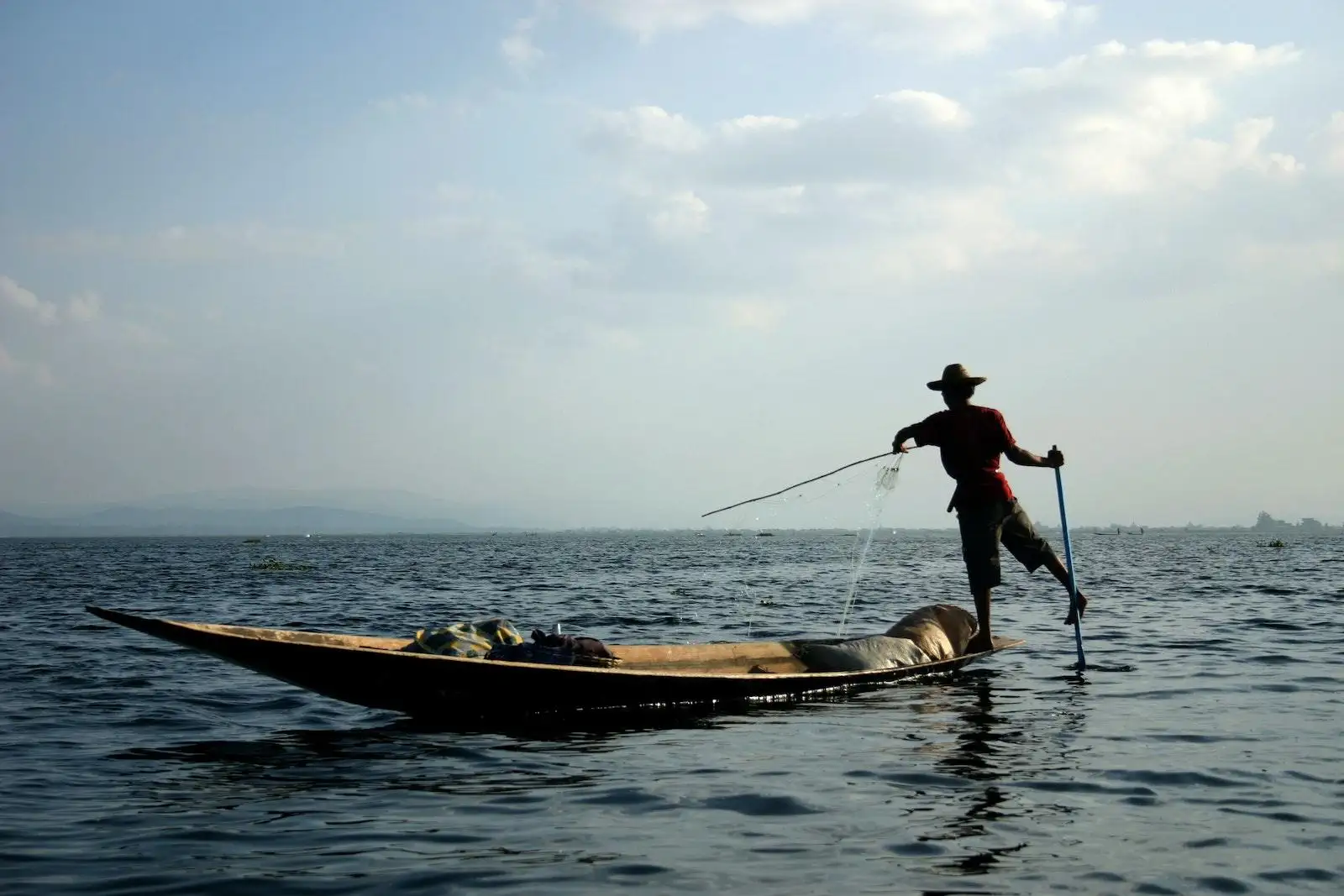 Man Standing on Brown Boat on Body of Water Under White and Blue Sky