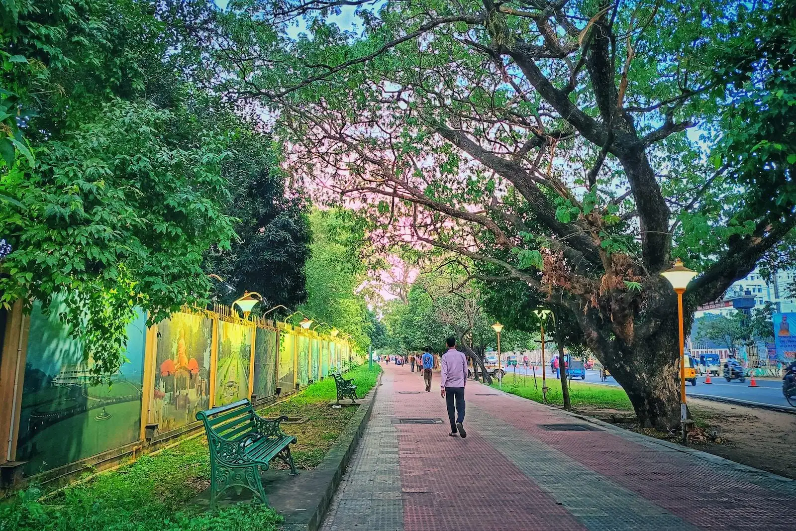 Photo by Sourav Debnath a woman walking down a sidewalk next to a green park bench