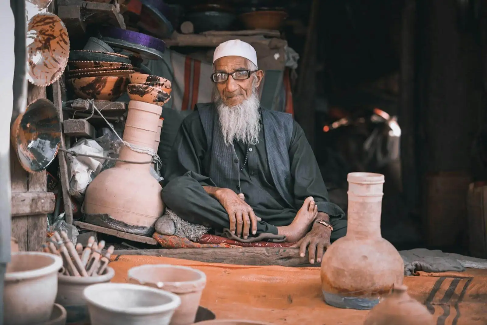 Photo by Sohaib Ghyasi man in gray long sleeve shirt sitting beside brown clay pots