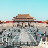 a group of people walking in a courtyard with Forbidden City in the background