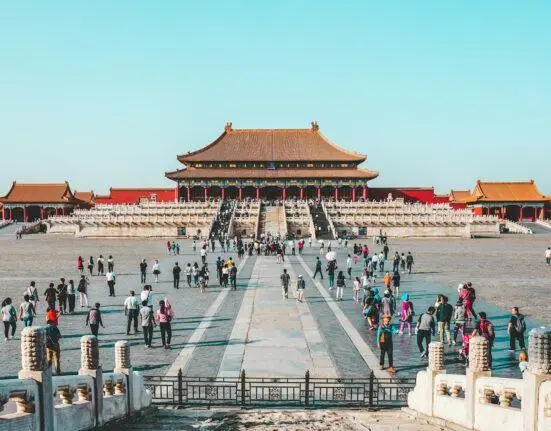 a group of people walking in a courtyard with Forbidden City in the background
