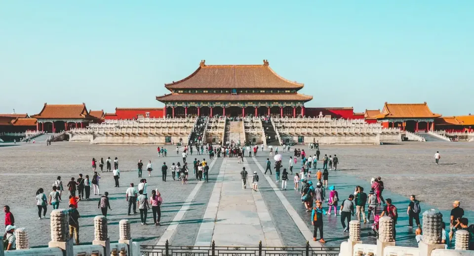 a group of people walking in a courtyard with Forbidden City in the background